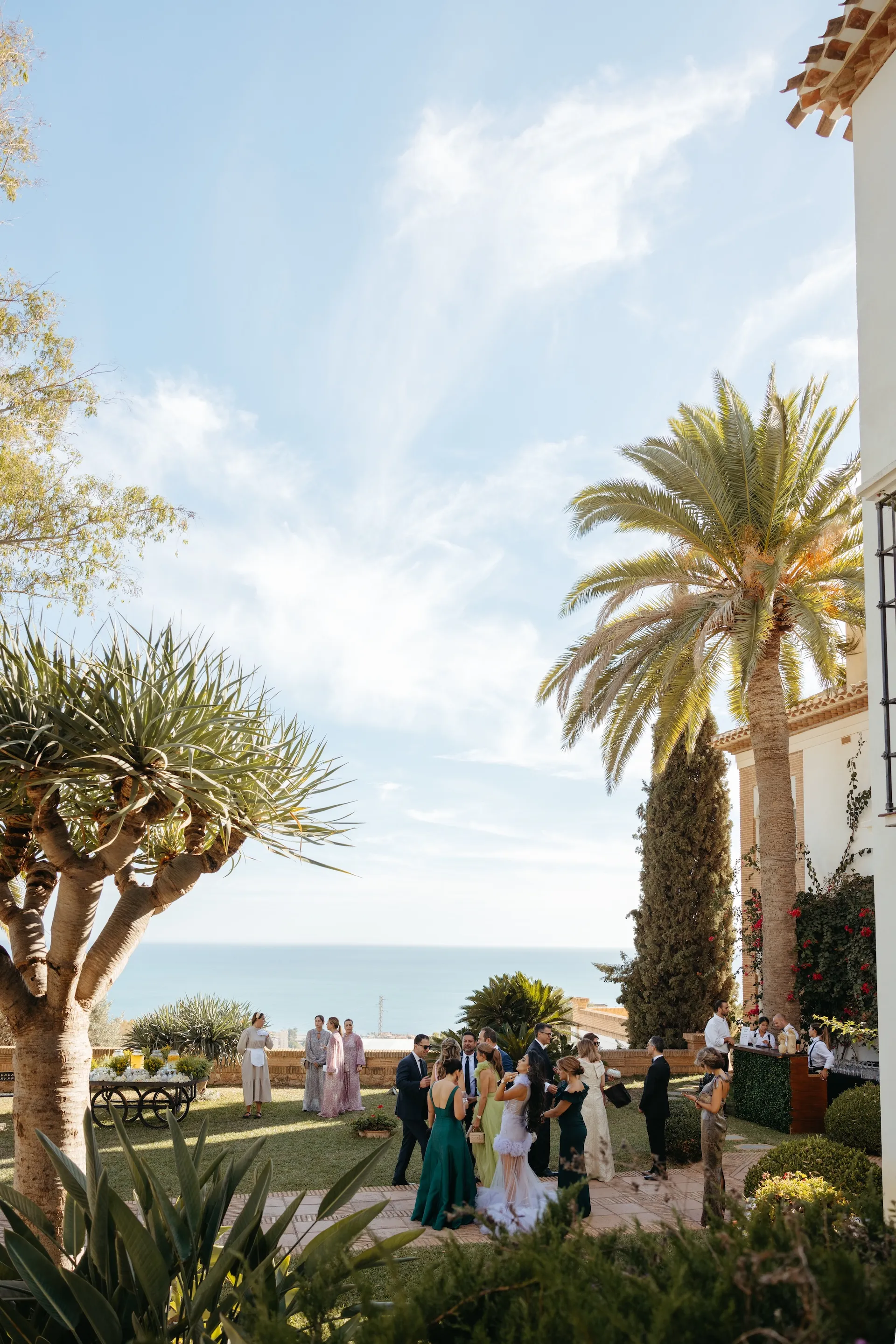 Wedding guests gathering in the gardens of a Mediterranean estate overlooking the sea