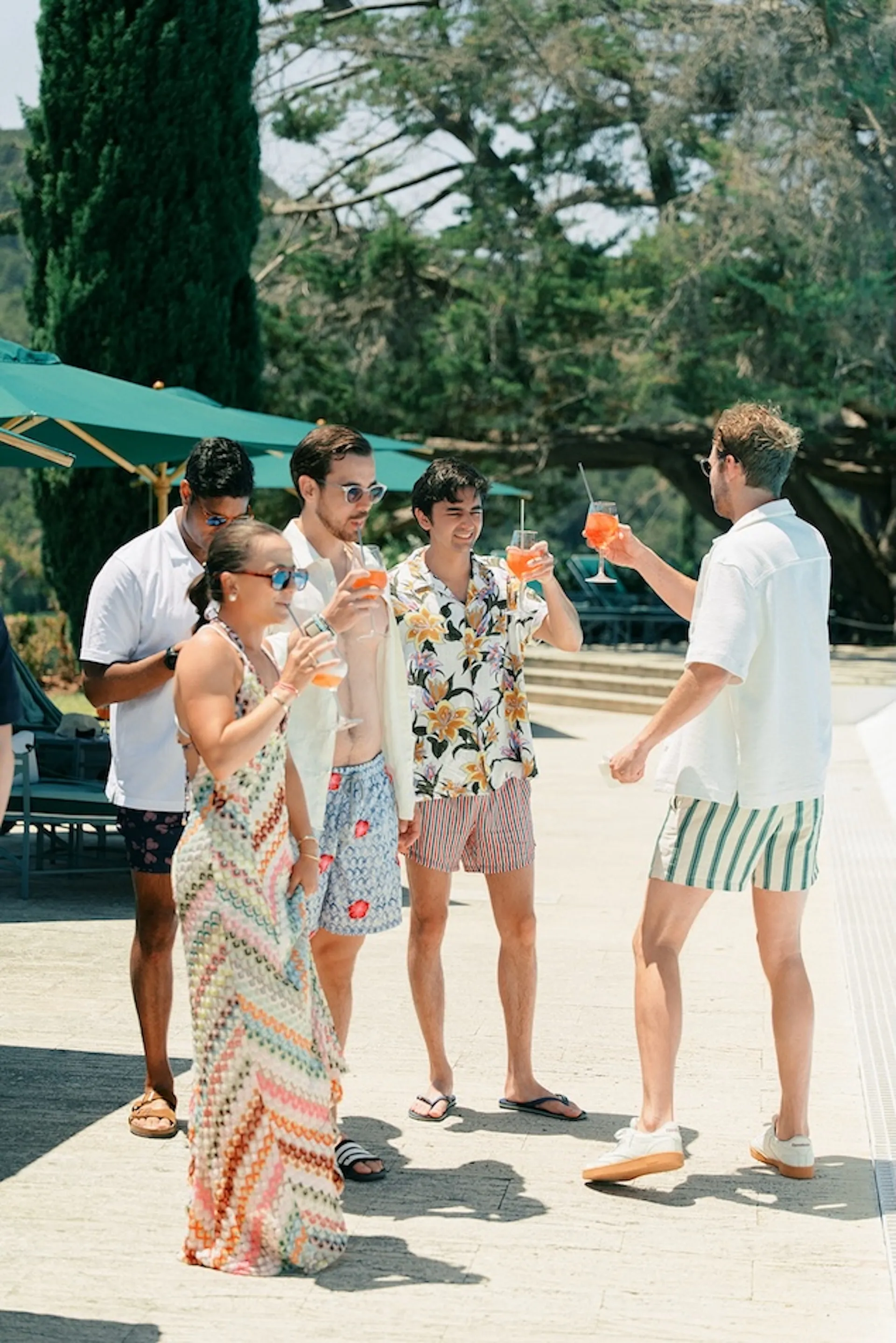 Guests in relaxed summer outfits raising drinks during a poolside wedding gathering