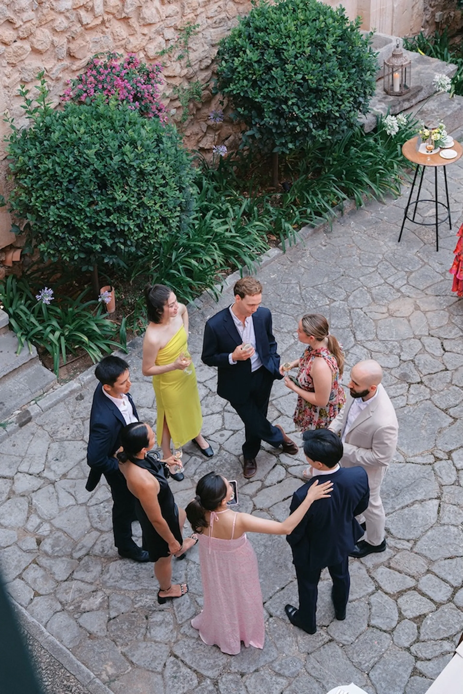 Guests in cocktail and formal attire socialising in a stone courtyard before the wedding